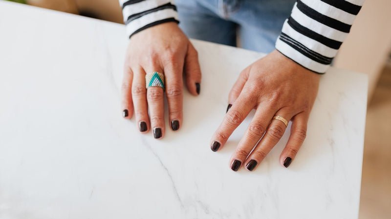 Hands with dark painted nails resting on a marble table