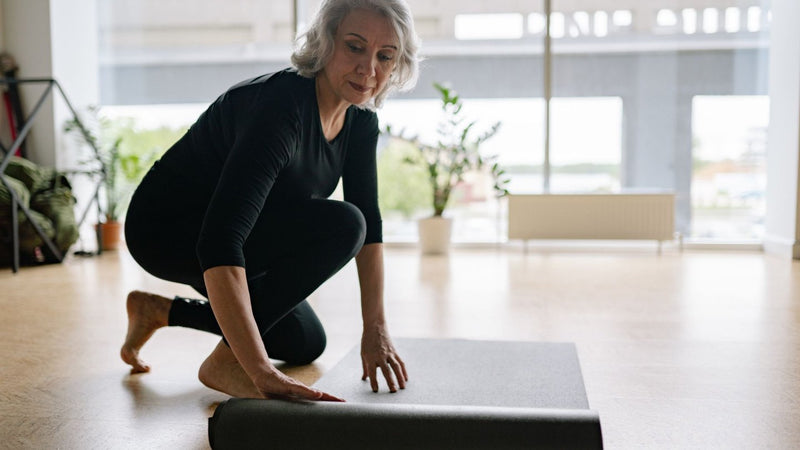Mature woman rolling out a yoga mat at home